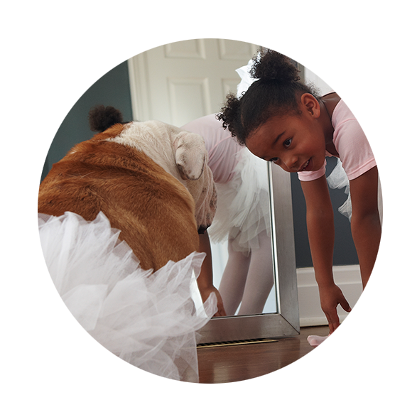 Girl in a ballerina outfit touching her toes looking up at her dog